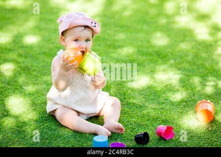 La bambina si siede in estate sul prato verde giocando in uno schema a piramide Foto Stock