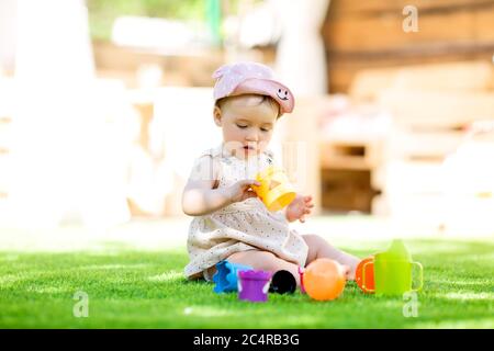 La bambina si siede in estate sul prato verde giocando in uno schema a piramide Foto Stock