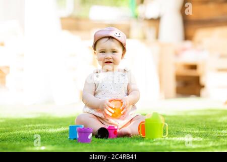 La bambina si siede in estate sul prato verde giocando in uno schema a piramide Foto Stock