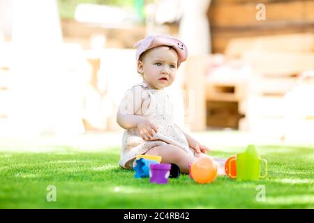 La bambina si siede in estate sul prato verde giocando in uno schema a piramide Foto Stock