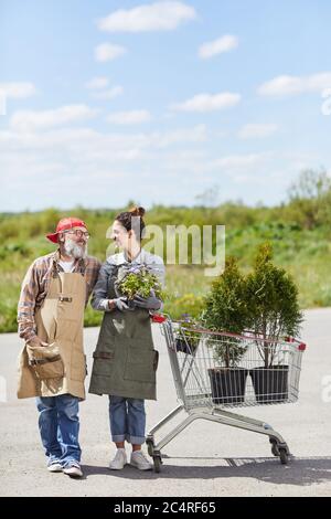 Verticale ritratto di lunghezza intera di due giardinieri che tengono vasi di fiori che si guardano l'un l'altro mentre si levano in piedi da carrello all'aperto, spazio di copia Foto Stock