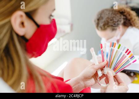 Donna che indossa maschera viso che controlla i colori per pedicure toenail Foto Stock