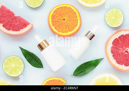 Flaconi contagocce bianchi con siero cosmetico e agrumi a fette. Cosmetici naturali con vitamina C. Vista dall'alto, piatto Foto Stock