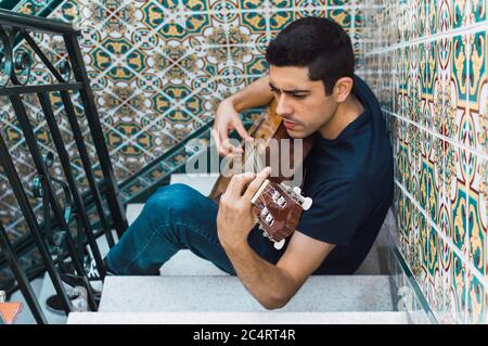 Mettere a fuoco l'uomo che suona la chitarra seduto su una scala con belle piastrelle. Foto Stock