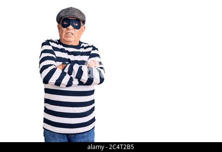 Uomo anziano bello che indossa maschera di scasso e t-shirt scettica e nervosa, disapprovando l'espressione sul viso con le braccia incrociate. Persona negativa. Foto Stock