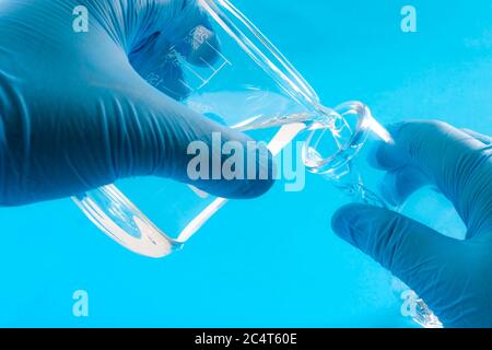 Esperimento scientifico, reazione chimica e concetto di chimica sperimentale con primo piano sulle mani di uno scienziato che indossa guanti di gomma blu e p Foto Stock