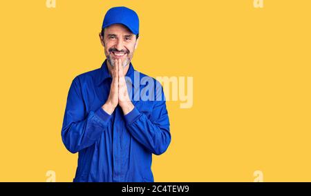 Bell'uomo di mezza età che indossa uniforme meccanica che prega con le mani insieme chiedendo perdono sorridente fiducioso. Foto Stock