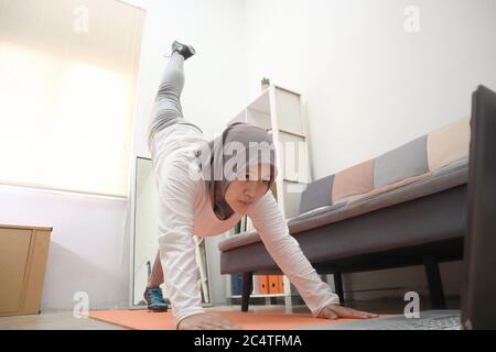 Donna musulmana asiatica che indossa hijab facendo esercizio a casa mentre si guarda video istruzione on-line sul laptop, concetto di allenamento domestico indoor, mantenere sano o Foto Stock