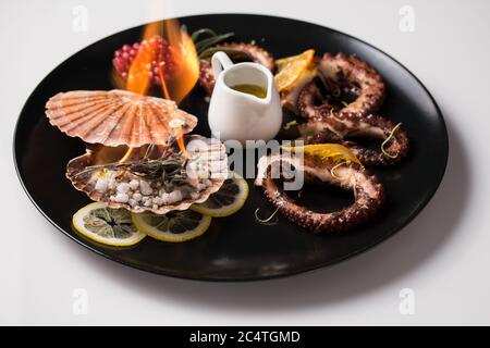 Bel piatto di polpo guarnito con limoni a fette e melograni una piastra nera Foto Stock