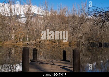 Bellissimo scatto di un lago riflettente con un molo di legno circondato da una fitta foresta Foto Stock