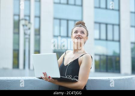 bella ragazza cammina per la città, lavorando su un computer portatile, tenendo un computer portatile e ascoltando musica. Foto Stock