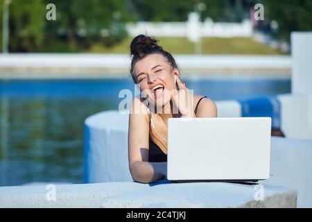 bella ragazza cammina per la città, lavorando su un computer portatile, tenendo un computer portatile e ascoltando musica. Foto Stock