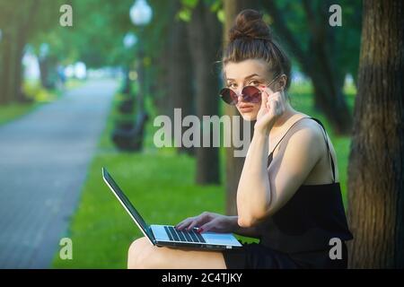bella ragazza cammina per la città, lavorando su un computer portatile, tenendo un computer portatile e ascoltando musica. Foto Stock