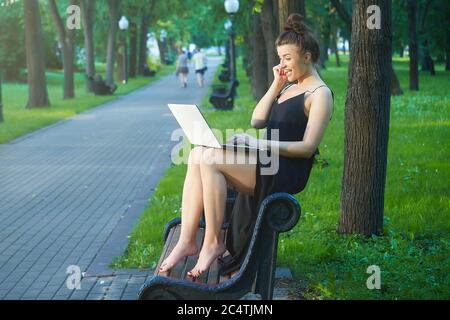 bella ragazza cammina per la città, lavorando su un computer portatile, tenendo un computer portatile e ascoltando musica. Foto Stock