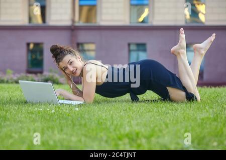 bella ragazza cammina per la città, lavorando su un computer portatile, tenendo un computer portatile e ascoltando musica. Foto Stock