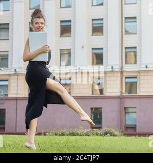 bella ragazza cammina per la città, lavorando su un computer portatile, tenendo un computer portatile e ascoltando musica. Foto Stock
