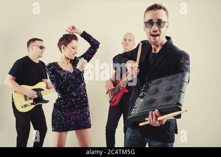 Eccitato giovane uomo che gioca su drum machine quando la sua band si esibisce in studio Foto Stock