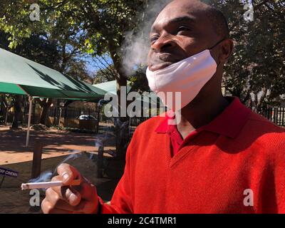 Johannesburg, Sudafrica. 27 Giugno 2020. Pocha Ngulube gode della sigaretta, che ha acquistato per 5 Rand (26 centesimi) - invece di 3 Rand (16 centesimi) - relativamente poco costoso sul mercato nero. In considerazione dei livelli di reddito e del forte aumento dei prezzi, le sigarette vengono di solito vendute singolarmente. Nella lotta contro il coronavirus, il governo sudafricano ha imposto alla fine di marzo uno dei più rigidi malfeuda del mondo, che include anche un divieto del tabacco. Credit: Ralf Krüger/dpa/Alamy Live News Foto Stock