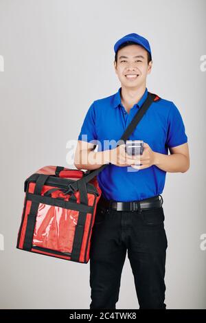 Ritratto di sorridente giovane corriere vietnamita con terminale di pagamento e borsa di consegna Foto Stock
