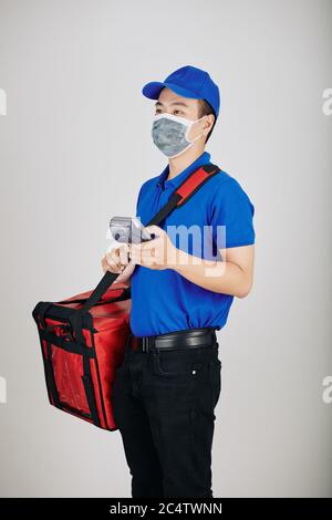 Servizio di consegna espresso in maschera medica con sacco di cibo grande e terminale di pagamento Foto Stock