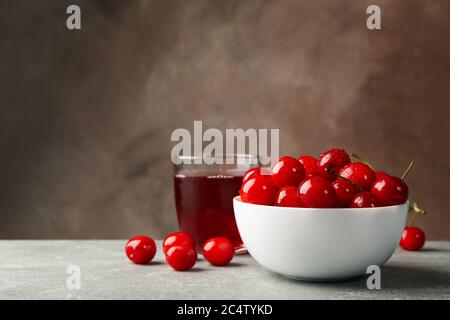 Ciotola con ciliegia rossa e bicchiere di succo sul tavolo grigio, spazio per il testo Foto Stock