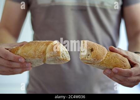 Le mani dell'uomo spezzano a metà il pane cotto Foto Stock