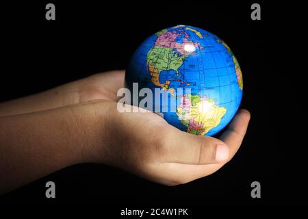 Mani di bambino che tengono il globo terrestre su sfondo nero. Globo terrestre isolato su sfondo nero. Mondo scolastico su sfondo nero. Foto Stock