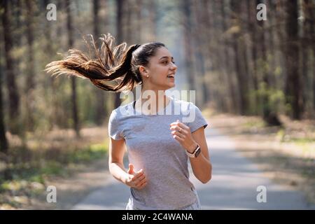 Bella giovane donna in esecuzione nel parco verde sulla soleggiata giornata estiva Foto Stock