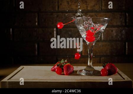 Ciliegie rosse di sangue che cadono nel cocktail su una tavola di legno Foto Stock