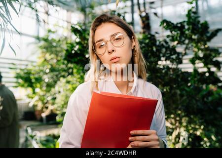 Giovane ingegnere agricolo che lavora in serra. Giovane scienziata femminile che guarda la macchina fotografica Foto Stock