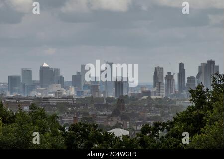 Londra, Regno Unito. 28 Giugno 2020. Vista della città di Londra e del Canary Wharf mentre si profilano in lontananza sul verde. La gente gode dei vari spazi di Hampstead Heath che si schivano tra forti docce a pioggia e intervalli di sole. Il "blocco" continua ad essere attenuato per l'epidemia di Coronavirus (Covid 19) a Londra. Credit: Guy Bell/Alamy Live News Foto Stock