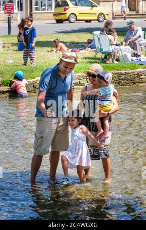 Bourton on the Water, Regno Unito. La gente gode del sole, pagaia nel fiume Windrush e si rilassa all'ombra, mentre il tempo continuo porta le persone all'aperto con l'allentamento delle restrizioni di blocco dovute a Covid-19 nel 2020. Foto Stock