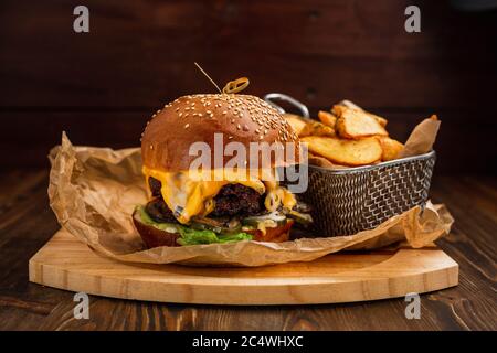 Cheeseburger doppio con patate fritte su tavola di legno Foto Stock