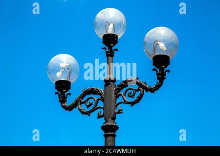 Lampione con una tripla lampada e tondo vetro trasparente sfumature contro il cielo blu. Foto Stock