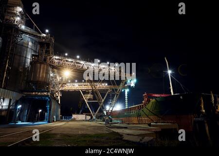 Big Grain terminal al porto. Trasporto alla rinfusa di cereali dal trasporto su strada alla nave durante la notte. Caricamento di prodotti di grano sulla nave da grandi elevatori a. Foto Stock