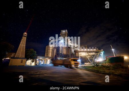 Terminale di grano al porto con cielo stellato sullo sfondo. Trasporto alla rinfusa di cereali dal trasporto su strada alla nave durante la notte. Caricamento dei prodotti a base di granella su Foto Stock