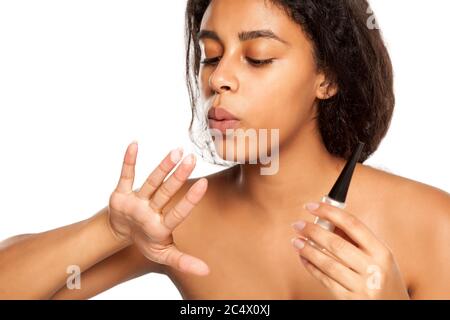 Giovane donna scura skinned asciugando la sua manicure su sfondo bianco Foto Stock