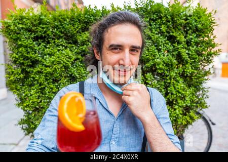 Ritratto maschile di giovane adulto che beve cocktail colorato al bar esterno con maschere facciali - nuovo concetto di stile di vita normale con gente felice tostatura drink Foto Stock