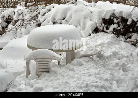 Dopo una caduta pesante, la neve scivola da un tetto di cottage e copre mobili da giardino in plastica Foto Stock