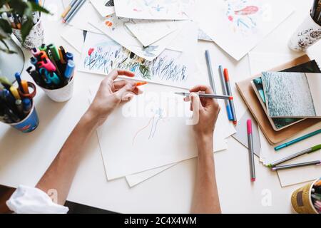 Primo piano disegno ragazza con pennarelli colorati su carta con foto e notepad sulla scrivania a casa isolato Foto Stock