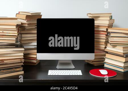 Computer da tavolo circondato da pile di libri sul tavolo. Concetto di studio online e preparazione agli esami. Foto Stock
