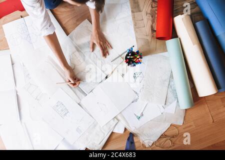 Primo piano le mani della ragazza disegnano schizzi sul pavimento con carta colorata whatman vicino a casa Foto Stock