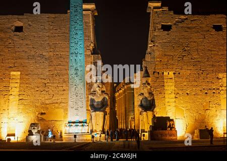 Grande statua e obelisco all'ingresso del pilone all'antico tempio egiziano di Luxor illuminato durante la notte Foto Stock