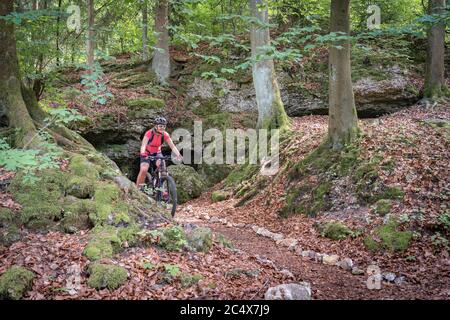 Ragazza adolescente che guida la sua mountain bike su un sentiero forestale di fronte a una grotta in Franconia Svizzera, Baviera, Germania Foto Stock