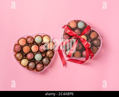 Caramelle al cioccolato tartufo fatto di cioccolato di diversi colori in una scatola a forma di cuore su sfondo rosa. Vacanza dessert Foto Stock