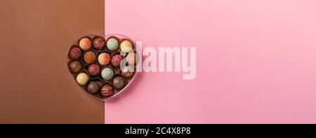 Caramelle al cioccolato tartufo fatto di cioccolato di diversi colori in una scatola a forma di cuore su sfondo rosa. Vacanza dessert Foto Stock