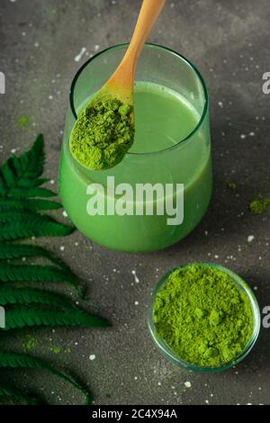 Fuoco selettivo, tè giapponese matcha verde con latte, con un cucchiaio di legno e fogliame su sfondo scuro Foto Stock