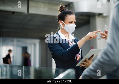 Assistente di volo che parla con un uomo d'affari in aeroporto, indossando la maschera facciale. Foto Stock