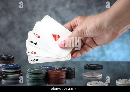 Primo piano di una mano donna che tiene carte da gioco di poker, con carte di quattro assi sullo sfondo. Gioco d'azzardo online. Dipendenza. Foto Stock
