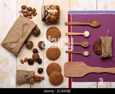 Ingredienti sani su sfondo di tessitura di legno chiaro. Sacchetto con noci, noci, cannella, biscotti, cucchiai di cacao, zucchero, sale, vista dall'alto. Spezie naturali, fogli di carta e nastri. Concetto di SPICE. Foto Stock